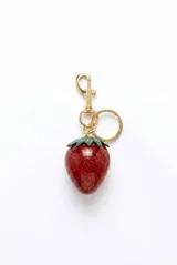 Llavero con dije en forma de frutilla de resina roja con glitter, coronada con hojas verdes esmaltadas. Incluye gancho mosquetón y argolla metálica dorada.