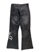 Jean de corte oxford y tiro bajo, color negro con efecto lavado. Presenta estampa bordada en la parte inferior de una de las piernas y detalles de costuras reforzadas en las rodillas.