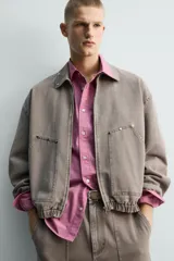 Cazadora de algodón de corte relajado, color marrón grisáceo con efecto lavado. Presenta cuello solapa con tachas metálicas, cierre frontal de cremallera, bolsillos de plastrón en la cadera y puños y bajo elásticos.