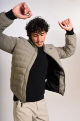 Campera puffer de corte clásico en color beige, con cierre frontal, cuello alto y puños elásticos. Presenta un diseño acolchado horizontal y un pequeño logo bordado en el pecho.