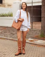 Bota de caña alta confeccionada en cuero color marrón tostado. Presenta un diseño con tres hebillas decorativas en la parte superior de la caña y una correa con hebilla y argolla metálica en el tobillo. Cuenta con suela plana y taco bajo de madera oscura.