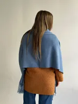 Ruana de tejido suave en color azul, con diseño de flecos en los extremos. Presenta una textura cálida y versátil para complementar diversos atuendos.