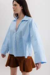 Camisa blanca de algodón, de corte holgado, con cuello clásico, mangas largas con puños anchos y un bolsillo de parche en el lateral.