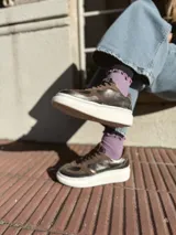 Zapatillas deportivas de cuero color peltre, con cordones negros y suela de goma blanca.