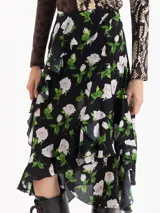 Pollera asimétrica de seda con estampado floral de rosas blancas sobre fondo negro. Presenta volados irregulares en forma de caracol que recorren el frente y la espalda, aportando volumen y movimiento.