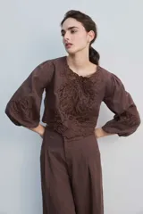 Blusa negra con detalles de apliques bordados en el pecho y las mangas, cuello redondo y mangas largas abullonadas.
