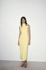 Vestido midi de cuello subido y sin mangas, confeccionado con un diseño drapeado lateral que aporta textura y movimiento a la prenda. Presenta un corte entallado y cierre de cremallera oculta en la espalda.