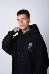 Buzo tipo canguro de corte oversize, color blanco, con capucha y cordones ajustables. Presenta un pequeño estampado de una rosa roja en el pecho y un bolsillo frontal tipo canguro.
