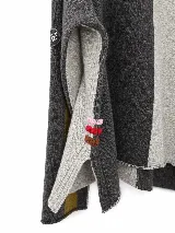 Polera de tejido lambswool con diseño bicolor en tonos neutros. Presenta cuello alto tejido, mangas largas con franjas laterales en color marrón y detalle de bordado artesanal con tres pequeñas líneas horizontales en colores vibrantes.