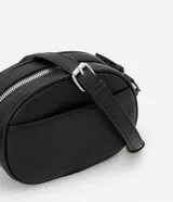 Cartera tipo camera bag pequeña, color marrón camel, de forma ovalada con superficie texturizada. Cuenta con correa ajustable larga, cierre principal con cremallera dorada y un pequeño bolsillo frontal con cremallera.