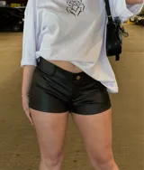 Mini short negro de cuero sintético, de tiro bajo, con cierre frontal de botón y presillas para cinto.