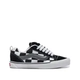Championes Vans Old Skool de caña baja, con diseño de tablero de ajedrez en blanco y negro, detalles en gamuza negra, franja lateral gris y cordones blancos.