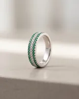 Anillo de plata con diseño de tres hileras, con circones blancos en el centro y piedras verdes en los laterales.