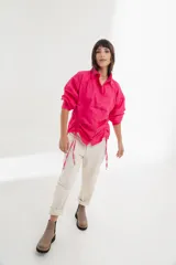 Camisa blanca de mangas largas con cuello clásico y cierre con botones. Presenta detalles de fruncido vertical en la parte delantera y cordones ajustables en los laterales. Corte holgado.