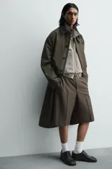 Bermuda de vestir color marrón oscuro, corte relajado y tiro alto, con pliegues frontales y cierre de botón y cremallera.