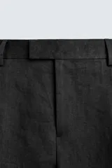 Pantalón de vestir regular fit confeccionado en lino, con pliegues frontales, bolsillos laterales y bolsillos traseros de doble vivo con botón. Presenta cierre frontal con cremallera y gancho metálico oculto.