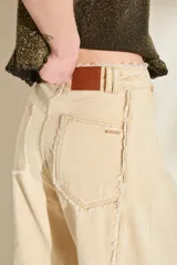 Jeans de corte wide leg, tiro alto y color beige, con detalles de costuras desflecadas a lo largo de las piernas.