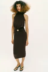 Vestido midi de cuello halter con detalle de drapeado en la cintura y broche metálico dorado en forma de caracola. Presenta cierre ajustable con lazadas en la espalda.