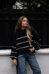 Buzo de tejido de punto en color bordó, con diseño de rayas horizontales formadas por pequeños triángulos blancos. Presenta cuello redondo, mangas largas con puños ajustados y un corte holgado.