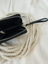 Billetera pequeña de cuero negro con textura de cocodrilo. Cuenta con cierre metálico perimetral y una correa de muñeca extraíble. Incluye compartimentos internos para billetes y un bolsillo con cierre para monedas.