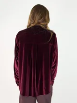 Camisa de terciopelo color bordó, con cuello mao y cierre frontal de botones. Presenta detalles de volados verticales a ambos lados de la botonera y mangas largas con puños abotonados.