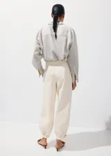 Pantalón jeans estilo balloon de tiro medio y largo tobillero, confeccionado en 100% algodón. Presenta detalle de pinzas en la cintura, dos bolsillos laterales, cierre de gancho y cremallera, y puños elásticos en los tobillos.