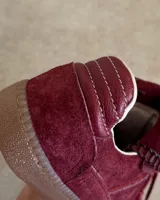 Sneakers bajas de cuero vacuno color bordó con suela marrón.