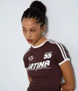 Remera de algodón color bordó con cuello redondo y bordes de mangas en color blanco. Presenta un diseño de estilo deportivo con estampado frontal que incluye el texto 'LATINA' y detalles de rayas blancas en los hombros.