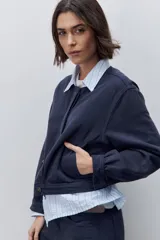 Campera azul marino de algodón, de corte relajado y largo corto, con cuello redondo, cierre frontal con botones metálicos, bolsillos delanteros y mangas largas con puños ajustables.