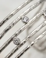 Esclava de acero con diseño calado y textura rugosa, decorada con pequeñas circonias incrustadas. El diseño simula múltiples aros superpuestos.