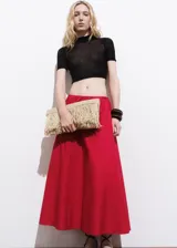 Falda larga color rojo, de tiro medio y diseño evasé, con bolsillos laterales y cierre de cremallera lateral.