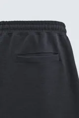 Bermuda estilo jogger de ajuste relajado, color negro, confeccionada en tejido interlock de algodón. Cuenta con cintura elástica ajustable mediante cordón, bolsillos delanteros tipo vivo y diseño liso.