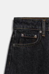 Jeans de tiro medio con corte tapered, confeccionados en denim de color negro con costuras en contraste. Presentan diseño de cinco bolsillos, trabillas en la cintura y cierre frontal con cremallera y botón.