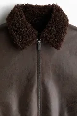 Campera de tejido revestido con acabado efecto cuero envejecido, cuello de solapa con forro de sherpa, cierre frontal y bolsillos laterales con cierre.