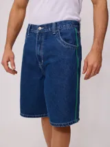 Bermuda de jean azul oscuro, corte holgado, con costuras en contraste color blanco y una franja lateral de ribete verde brillante.