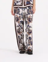 Pantalon de corte recto y holgado con estampado floral en tonos azules, marrones y crema. Presenta una franja lateral vertical en color marrón oscuro y cierre lateral.