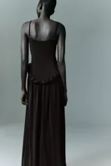 Vestido largo de color negro con escote recto y tirantes finos ajustables. Presenta un diseño con detalle de volados en la cintura que genera un efecto peplum y una falda con caída fluida.