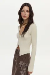 Cardigan tejido en rib con hilado de lurex, color crudo, calce al cuerpo, cuello polo, mangas largas con aberturas y cierre metálico frontal bidireccional.