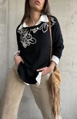 Sweater negro con diseño bordado en hilo crudo en el escote y el hombro, de manga larga y calce holgado.