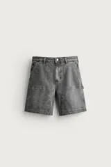 Bermuda de denim estilo carpintero en color gris con efecto lavado, corte relaxed fit, bolsillos laterales aplicados y cierre frontal con cremallera y botón.