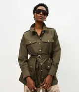 Campera parka Marfinno verde militar de sarga de algodón, con cuello camisero, bolsillos utilitarios con solapa en el pecho y los costados, cierre frontal con botones dorados y cinturón incorporado con hebilla metálica.