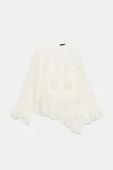 Camisa de cuello redondo y manga larga color blanco crudo, con múltiples capas de volantes horizontales en el frente y bajo asimétrico. Cierre trasero con abertura y botón.