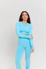 Conjunto deportivo de dos piezas color turquesa, compuesto por un top de manga larga con cuello redondo y detalle de textura en el pecho, y calzas de tiro alto. Ambas prendas presentan un diseño sin costuras con detalles texturizados y logo estampado en el top.