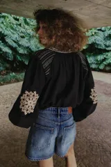 Camisa negra de manga larga con cuello redondo y escote en V, adornada con bordados florales en contraste en tonos beige y marrón a lo largo de la abertura frontal, hombros y mangas.