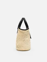Bolso tipo canasto Jacquemus Le Panier Soli tejido en fibra vegetal de color natural, con asas cortas, detalles y bolsillo frontal de cuero negro con el logotipo de la marca en letras doradas.