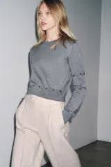 Jersey de punto de cuello redondo y manga larga, con diseño cropped. Presenta detalles de costuras con botones que permiten desmontar partes de la prenda en las mangas y en la cintura.