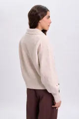 Buzo de punto beige con cuello polo y mangas largas, confeccionado con mezcla de lana y elastano.