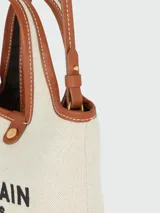 Bolso tote Balmain de lino color crudo con logo estampado en negro y detalles en cuero marrón.