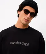 Remera de manga larga Blue Steel, color negro, con diseño de cuello redondo y corte relajado. Presenta un estampado frontal con la palabra 'WORLDWIDE' en letras blancas y detalles de líneas horizontales en contraste.