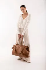 Bolso de viaje tipo weekender de cuero color marrón con doble asa de mano y correa bandolera ajustable y desmontable.